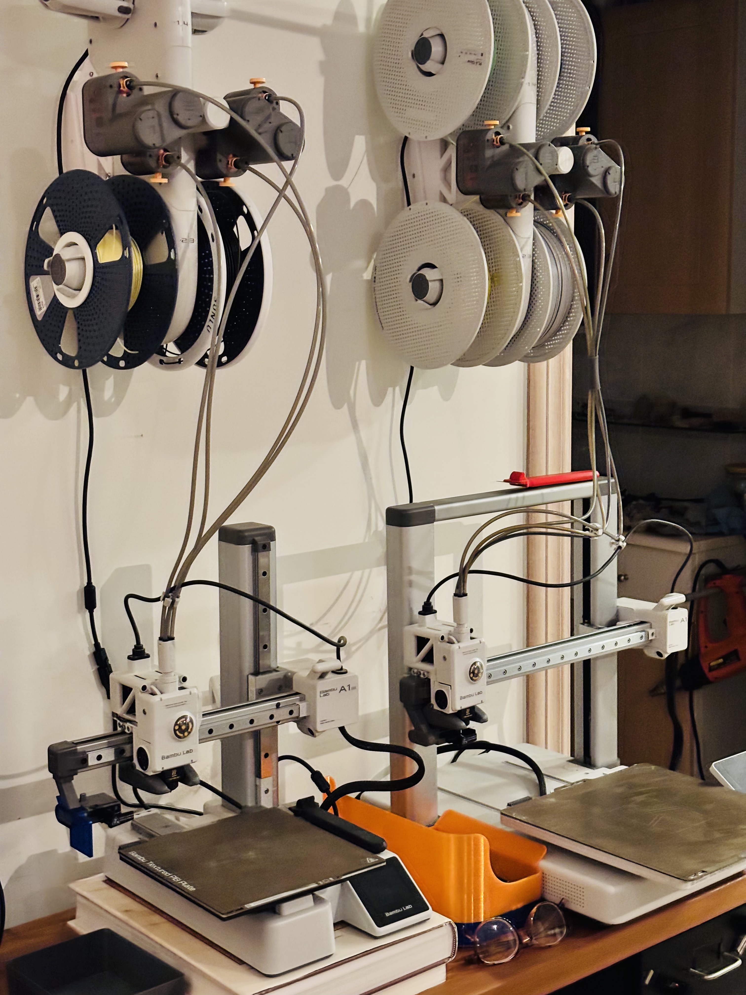 Zwei Bambu Lab A1 Mini-Drucker auf einer Werkbank mit darüber angebrachten, an der Wand montierten Filamentrollen.